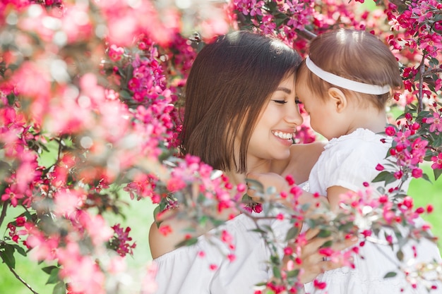 Retrato de uma jovem mãe linda com sua filhinha. close-up ainda de amar a família. mulher atraente, segurando seu filho em flores cor de rosa e sorrindo. Foto Premium