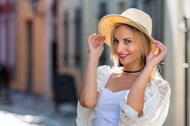 Retrato de uma linda mulher loira com chapéu de sol, vestido com roupas leves. menina na moda posando no fundo da rua Foto Premium