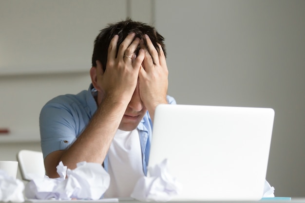 Retrato do homem perto do laptop, as mãos fechando o rosto Foto gratuita