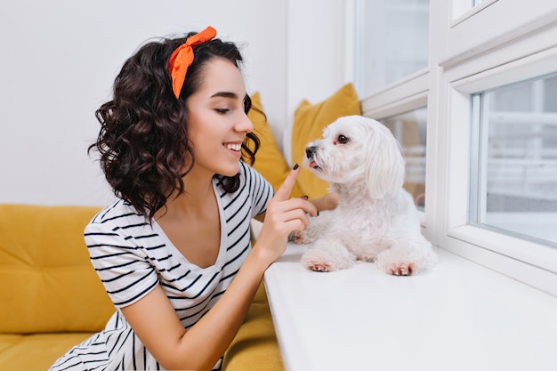 Retrato incrível alegre elegante jovem brincando com o cachorrinho no apartamento moderno. divertindo-se com animais domésticos, sorrindo, bom humor, em casa Foto gratuita