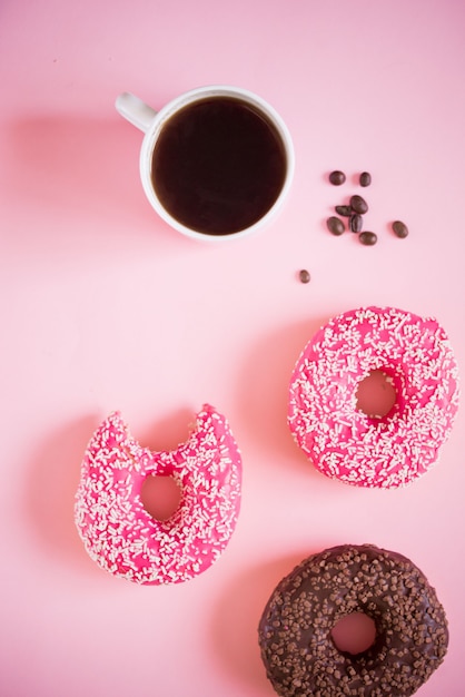 Rosquinhas saborosas e deliciosas com glacê rosa e pó com uma xícara de café aromático em uma superfície branca Foto Premium