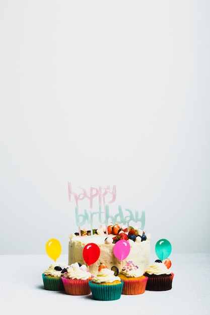 Saboroso bolo fresco com frutas e feliz aniversário título perto conjunto de bolinhos Foto gratuita