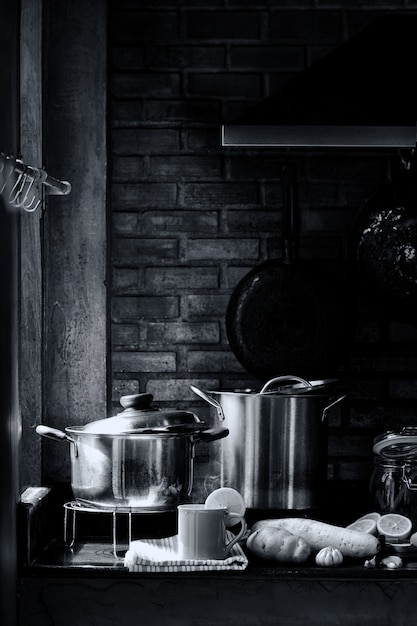 Sala de cozinha com utensílios de cozinha, fogão, exaustor e parede de tijolos com uma xícara de chá de limão com vapor e vapor. conceito da vida do amante do cozinheiro chefe ou do cozinheiro. imagem preto e branca retrô. Foto Premium