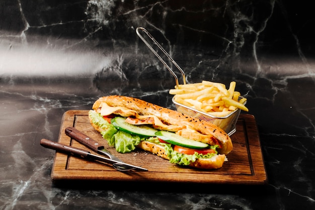 Sanduíche de baguete com ingredientes misturados e batatas fritas em uma placa de madeira. Foto gratuita