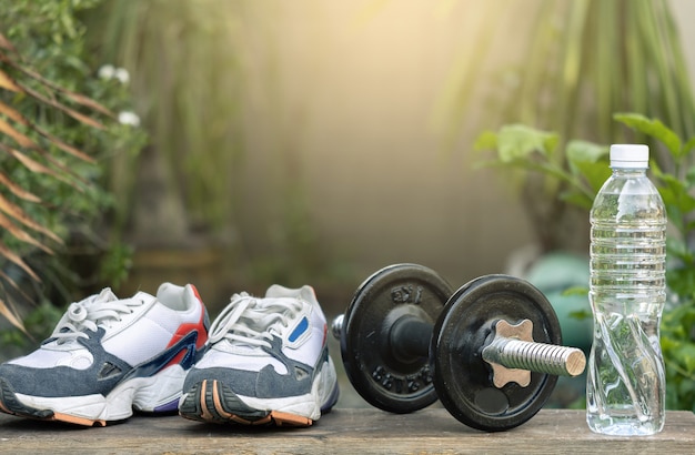 Sapatas dos esportes com pesos do dumbbell e garrafa na árvore borrada. metaphor fitness and workout concept exercise estilo de vida de saúde muscular Foto Premium