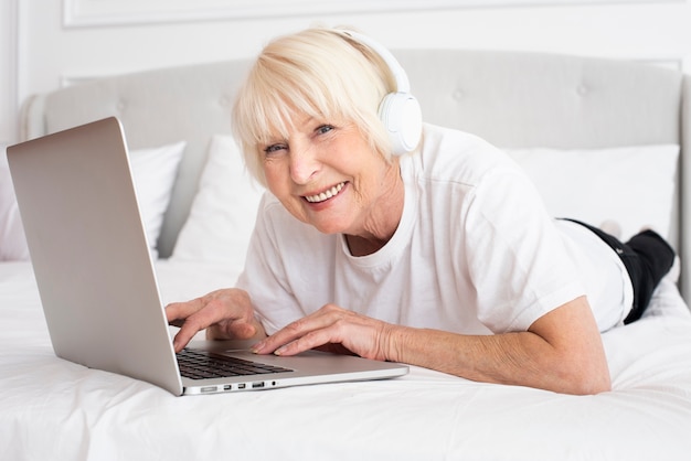 Sênior sorridente com fones de ouvido e laptop Foto gratuita