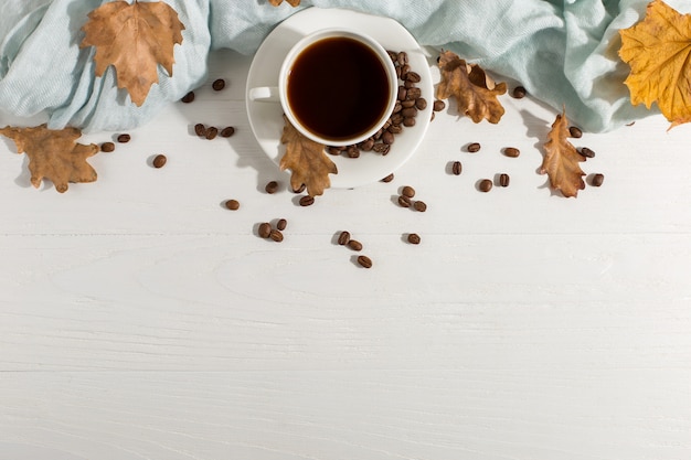 Seque as folhas amarelas, lenço azul, grãos de café e uma xícara em uma mesa branca, dia de início de manhã. fundo do humor do outono, copyspace, configuração lisa. Foto Premium