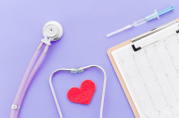Seringa; relatório médico na área de transferência; coração com estetoscópio no fundo roxo Foto gratuita