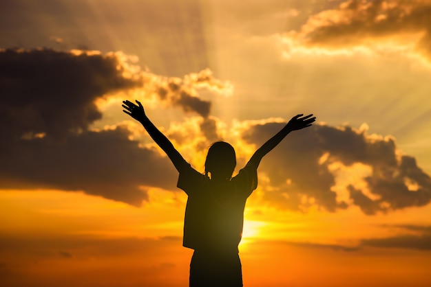 Silhueta de mulher feliz abre os braços no campo de trigo ao pôr do sol Foto Premium