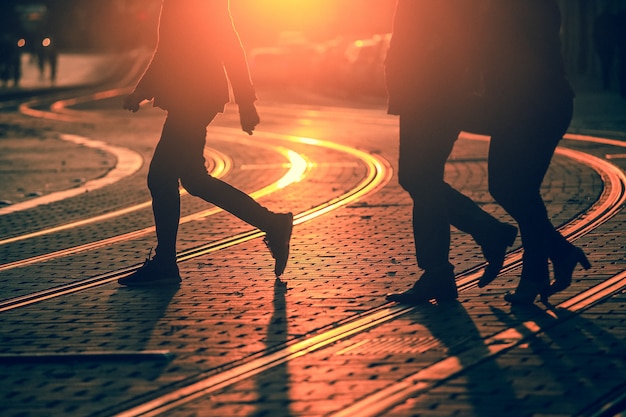 Silhuetas de pessoas andando na rua da cidade e lançando sombras no pavimento com trilhos em bordeaux, textura de grão aplicar Foto Premium