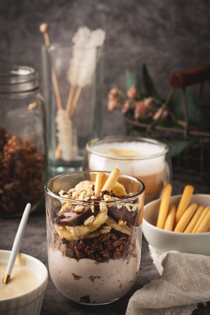 Sobremesa em um copo de iogurte, granola, banana e chocolate com biscoitos, café cappuccino. Foto Premium