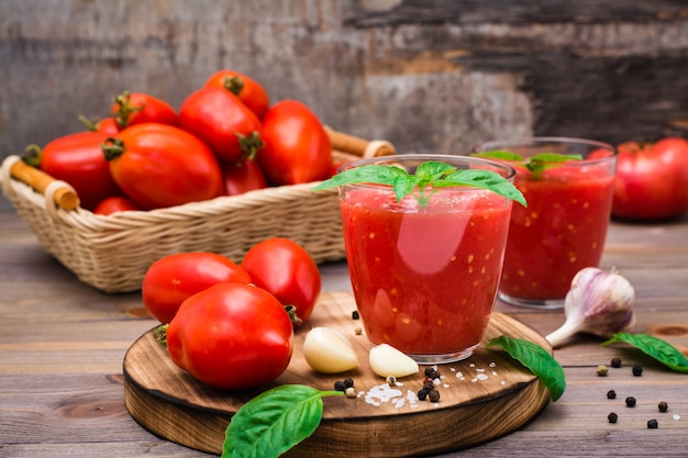 Suco de tomate fresco com folhas de manjericão em copos e tomates em uma mesa de madeira Foto Premium