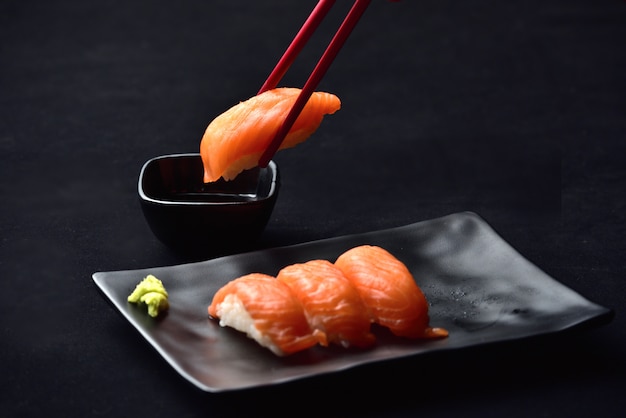 Sushi do nigiri e molho salmon do wasabi com os chopsticks no valvet preto. Foto Premium