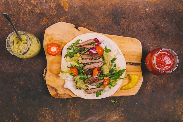 Tacos mexicanos com carne bovina; legumes frescos e guacamole com molho de salsa no fundo enferrujado Foto gratuita