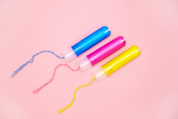 Tampões de algodão do ciclo menstrual três com applicartors amarelos cor-de-rosa azuis no rosa Foto Premium