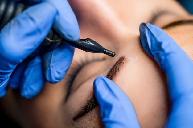 Tatuagem de maquiagem permanente nas sobrancelhas no salão de beleza. mulher com as sobrancelhas coloridas. maquiagem semi-permanente para sobrancelhas. Foto Premium