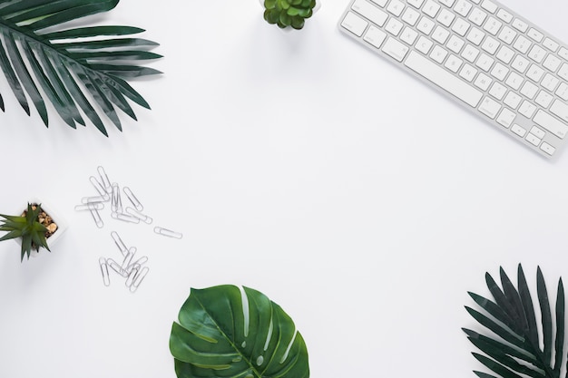 Teclado; cactos; folhas e clipes de papel na mesa branca com espaço de cópia para escrever texto Foto gratuita