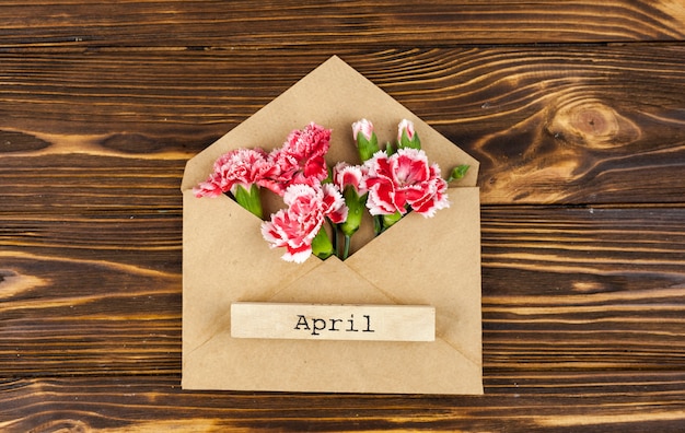 Texto de abril no envelope com flores vermelhas na mesa Foto gratuita
