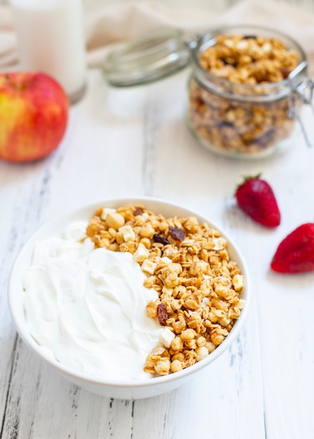 Tigela de granola caseira com iogurte grego. ingredientes para um café da manhã saudável - granola, maçã, morango e leite. fechar-se Foto Premium