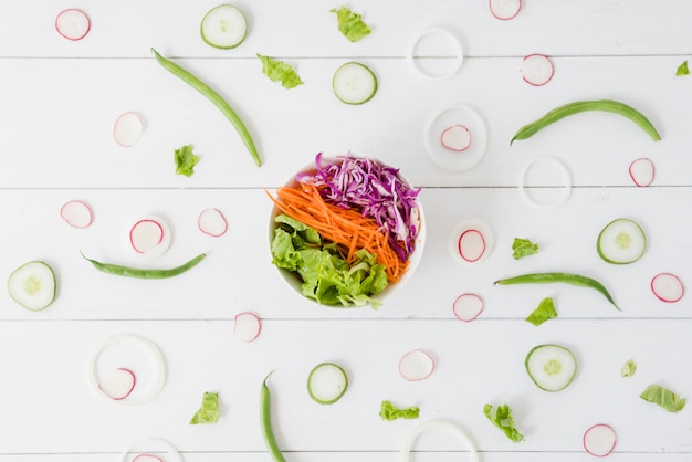 Tigela de salada espalhada com nabo; pepino; fatias de cebola com feijão verde na mesa de madeira Foto gratuita