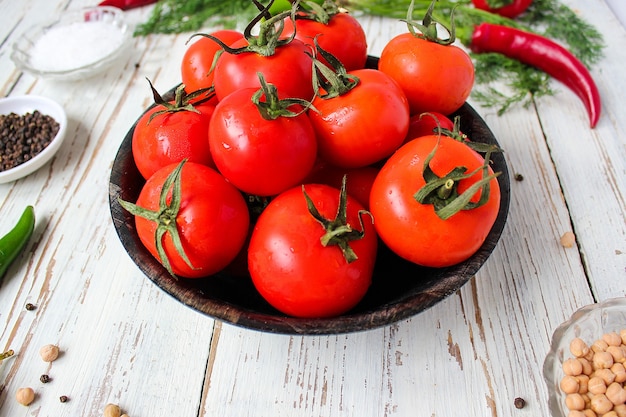 Tomates vermelhos orgânicos frescos em chapa preta na mesa de madeira branca com verde e vermelho e pimenta, pimentão verde, pimenta preta, sal, close-up, conceito saudável Foto gratuita