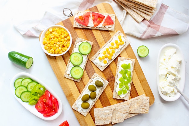Torrada caseira com queijo cottage e azeitonas verdes, fatias de repolho, tomate, milho, pimenta verde na tábua. conceito de comida saudável, vista superior. configuração plana Foto gratuita