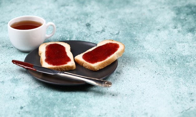 Torradas de café da manhã com geléia de morango em uma placa preta e uma xícara de chá. Foto gratuita
