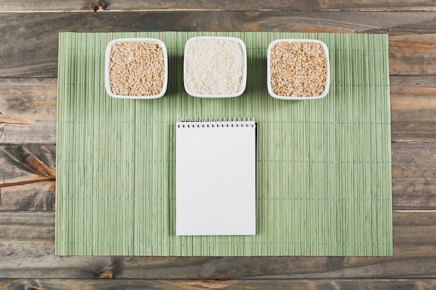 Três, diferente, tipo, de, cru, arroz, bacias, com, espiral, notepad, ligado, verde, placemat, sobre, a, tabela Foto gratuita