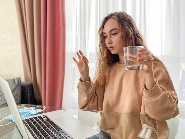 Triste, chateada, jovem mulher segurando um copo de água e pílulas sentado na sala de estar, sentindo-se doente Foto Premium