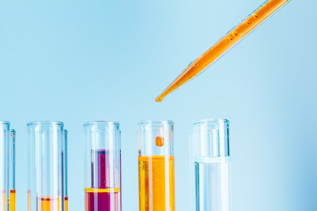 Tubos de ensaio de laboratório com líquidos vermelhos e amarelos sobre fundo azul claro Foto Premium