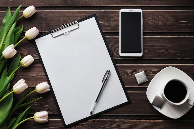 Tulipas brancas em uma mesa de madeira com um tablet de papel vazio e smartphone e uma xícara de café Foto Premium