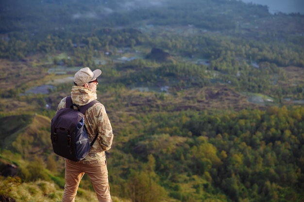 Turista de homem olha para o nascer do sol no vulcão batur, na ilha de blai, na indonésia. homem alpinista com mochila viajar no topo do vulcão, conceito de viagens Foto Premium
