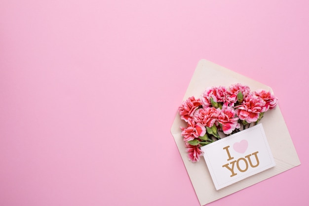 Um envelope com flores cor de rosa e um cartão eu te amo em rosa Foto Premium