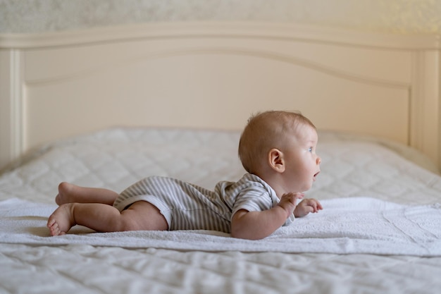 Um pequeno bebê recém nascido engatinha na cama e levanta a cabeça