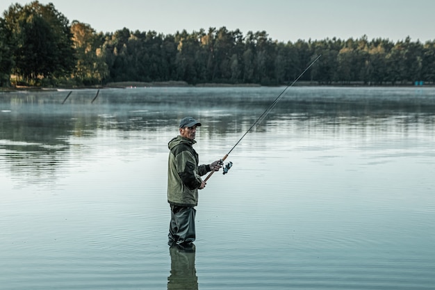 Um pescador no lago está de pé na água e pescando uma vara de pescar férias de hobby na pesca Foto Premium