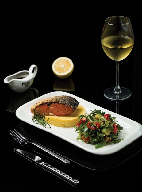 Um prato de filé de salmão grelhado com especiarias e salada verde, servido com um copo de vinho italiano Foto gratuita