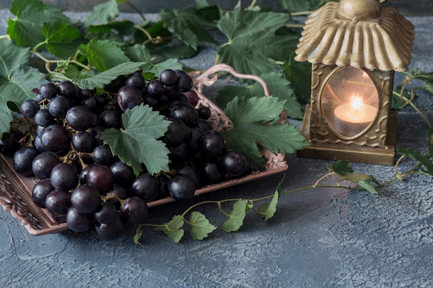 Um uvas escuras em um vaso de bronze e um castiçal de ouro com uma vela Foto Premium