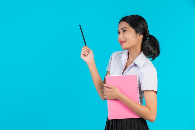 Uma estudante asiática com a com seu caderno rosa em um azul. Foto gratuita
