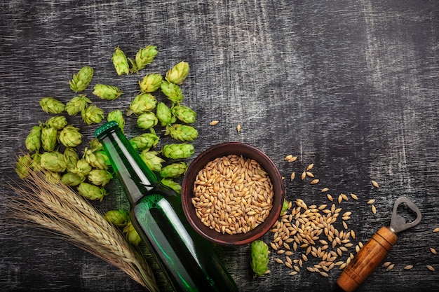 Uma garrafa de cerveja com lúpulo verde, aveia, espigas de trigo e abridor na placa de giz preto riscado Foto Premium