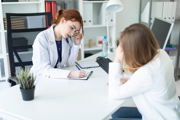 Uma linda garota vestida de branco está sentada à mesa do escritório e se comunicando com o interlocutor. a menina faz anotações na folha. Foto Premium