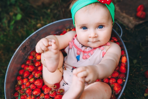 Uma menina banha-se em uma bacia com as morangos no jardim. Foto Premium