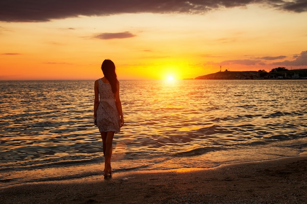 Uma Mulher Esbelta Fica Na Praia Assistindo O Pôr Do Sol O Pôr Do Sol Vai No Horizonte Para O 9744