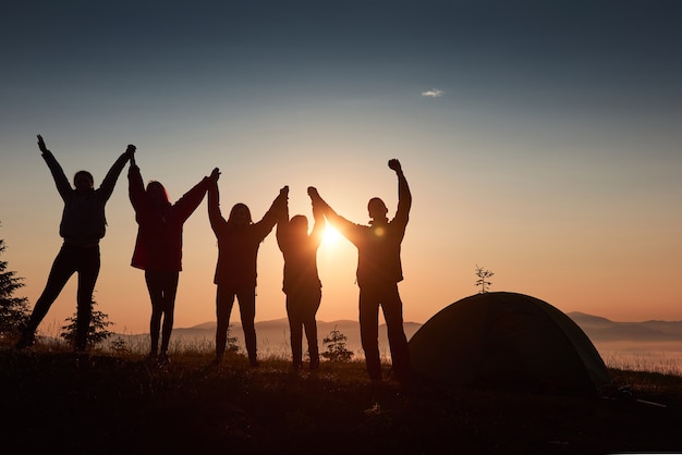 Uma silhueta de um grupo de pessoas se diverte no topo da montanha perto da tenda durante o pôr do sol. Foto gratuita