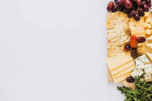 Variedade de fatias de queijo e cubos com uvas, tomate e salsa no fundo branco Foto gratuita