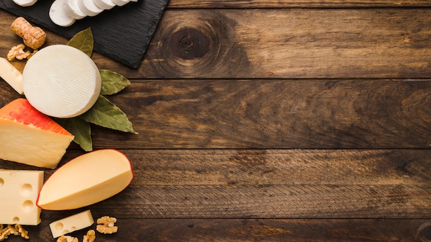 Vários deliciosos queijos com folhas de louro e noz na madeira texturizada Foto gratuita