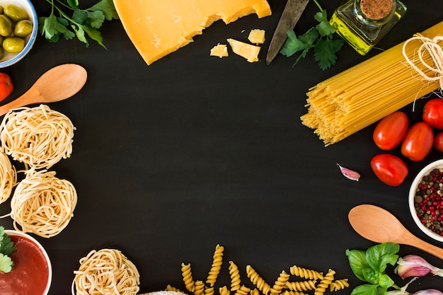 Vários tipos de macarrão seco com legumes e ervas em fundo preto Foto gratuita