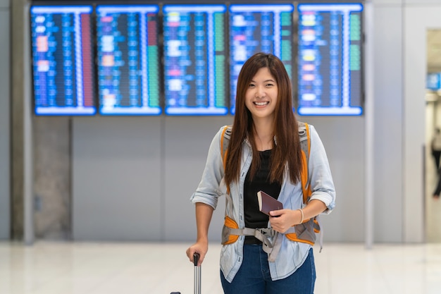 Viajante asiático com bagagem com passaporte andando sobre a placa de voo para check-in Foto Premium