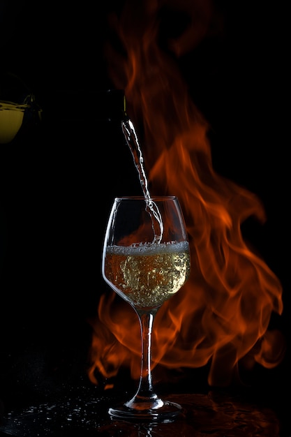 Vinho branco está sendo derramado em vidro com haste longa em backgrond escuro com fogo Foto gratuita