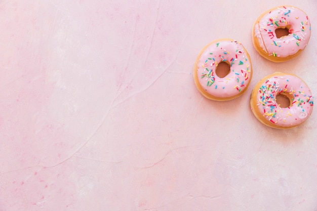 Visão aérea de donuts frescos com chuviscos em pano de fundo rosa Foto gratuita