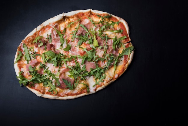 Visão aérea de pizza com bacon e rúcula no balcão da cozinha preto Foto gratuita
